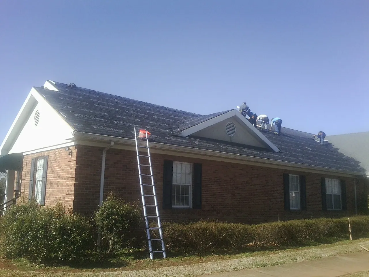 Crew tearing shingles off a brick ranch roof with a ladder set — Metal Roof Repair work by our crew in Milledgeville