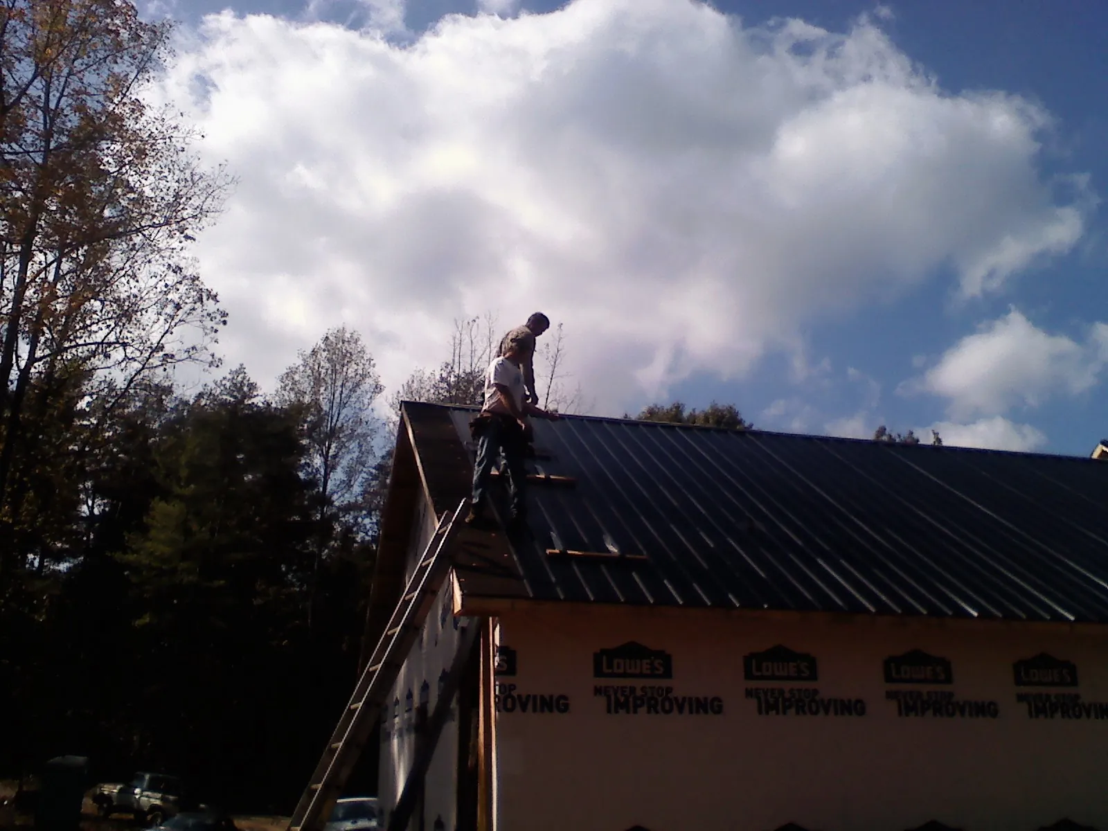Roofer fastening dark metal panels high against a cloudy sky, from a Roof Inspection job in Milledgeville