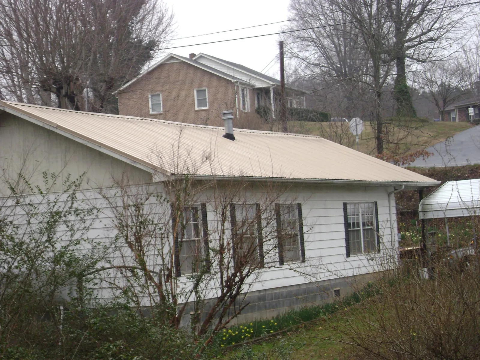 Tan metal roof on a white sided house set into a hillside — Commercial Roofing by Roofing Brothers in Milledgeville